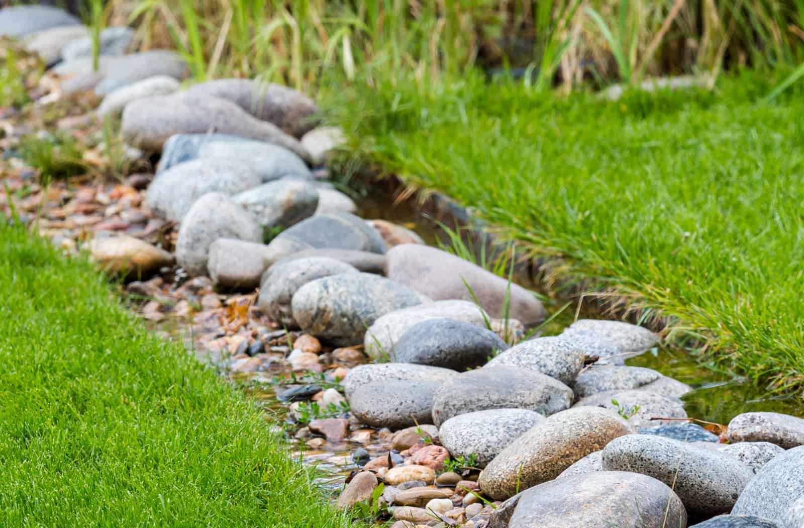 French drain installation in a back yard, water channeled through buried pipe under rocks